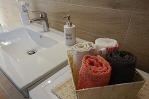 Un baño con lavamanos blanco, grifo plateado, una botella de jabón y una cesta de toallas.