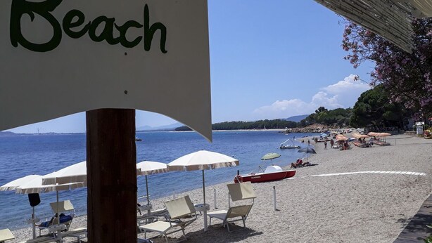 A beach with umbrellas, lounge chairs, and a sign reading "Beach". - Casa Selvaggio Blu (Baunei)