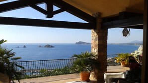 A terrace with wicker furniture, potted plants, and a view of the sea and islands. - Casa sul Porto (Baunei)