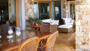 A stone-walled dining area with wicker furniture and a glass table. - Casa sul Porto (Baunei)