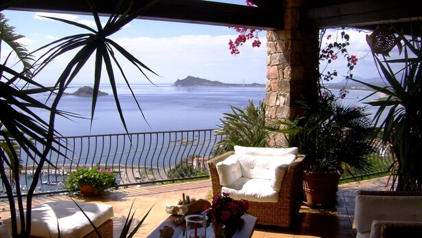 A balcony with a view of the sea, wicker furniture, and potted plants. - Casa sul Porto (Baunei)