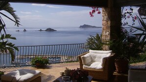 A balcony with a wicker sofa, potted plants, and a view of the sea and boats. - Casa sul Porto (Baunei)