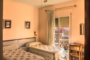 Een slaapkamer met twee bedden, een raam met gordijn, een stoel en een klein tafeltje.
