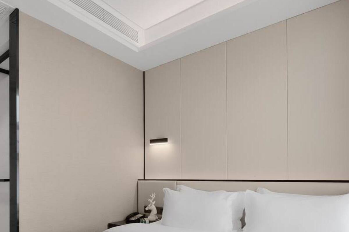 Ein modernes Hotelzimmer mit einem großen Bett, einem Nachttisch mit Telefon und einer an der Wand befestigten Lampe.