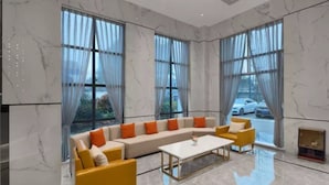 A modern living room with a beige sectional sofa, yellow armchairs, and a white coffee table. Large windows with sheer curtains offer views of the street. - Vyluk Hotel Chengdu UESTC (Chengdu)