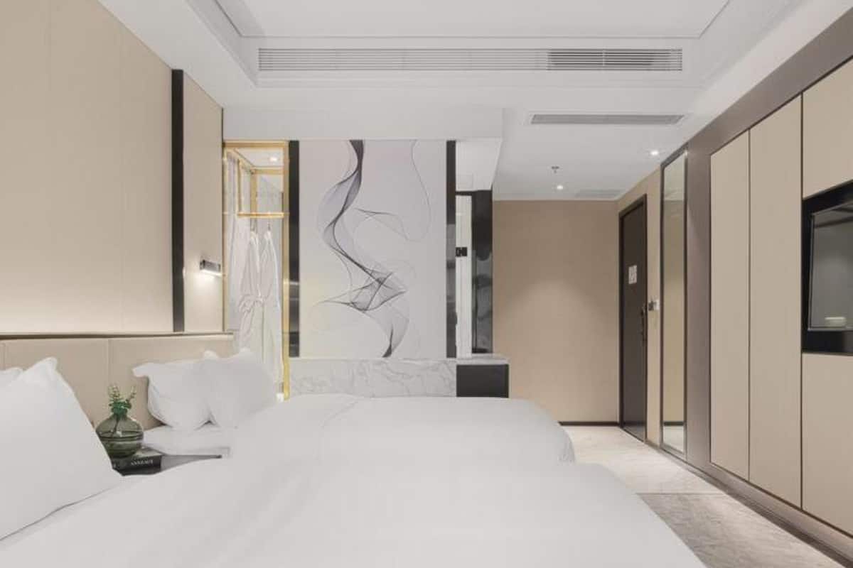 Ein modernes Hotelzimmer mit einem großen Bett, einem Nachttisch, einem an der Wand montierten Fernseher und einem Kleiderschrank.