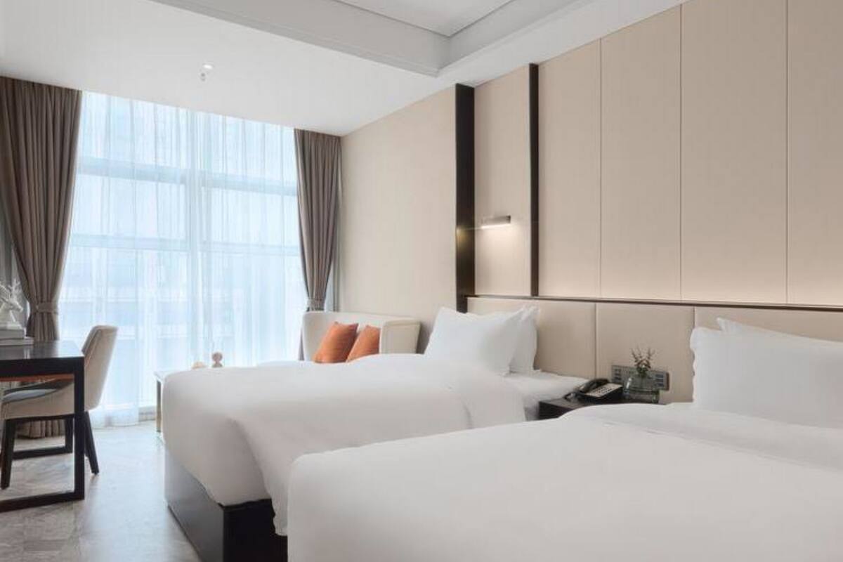 Ein Hotelzimmer mit zwei Betten, einem Schreibtisch und einem großen Fenster mit Vorhängen.