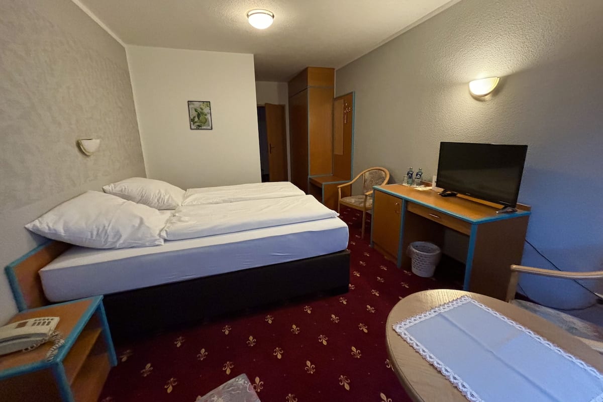 A hotel room with a bed, a desk with a television, a chair, and a small table with a telephone.