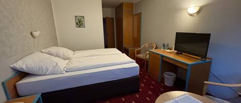 Habitación de hotel con cama, escritorio con televisor, una silla y una mesita con teléfono.