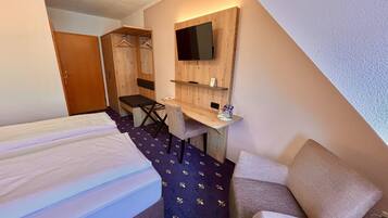 Habitación de hotel con cama, escritorio, silla, televisor montado en la pared y armario.