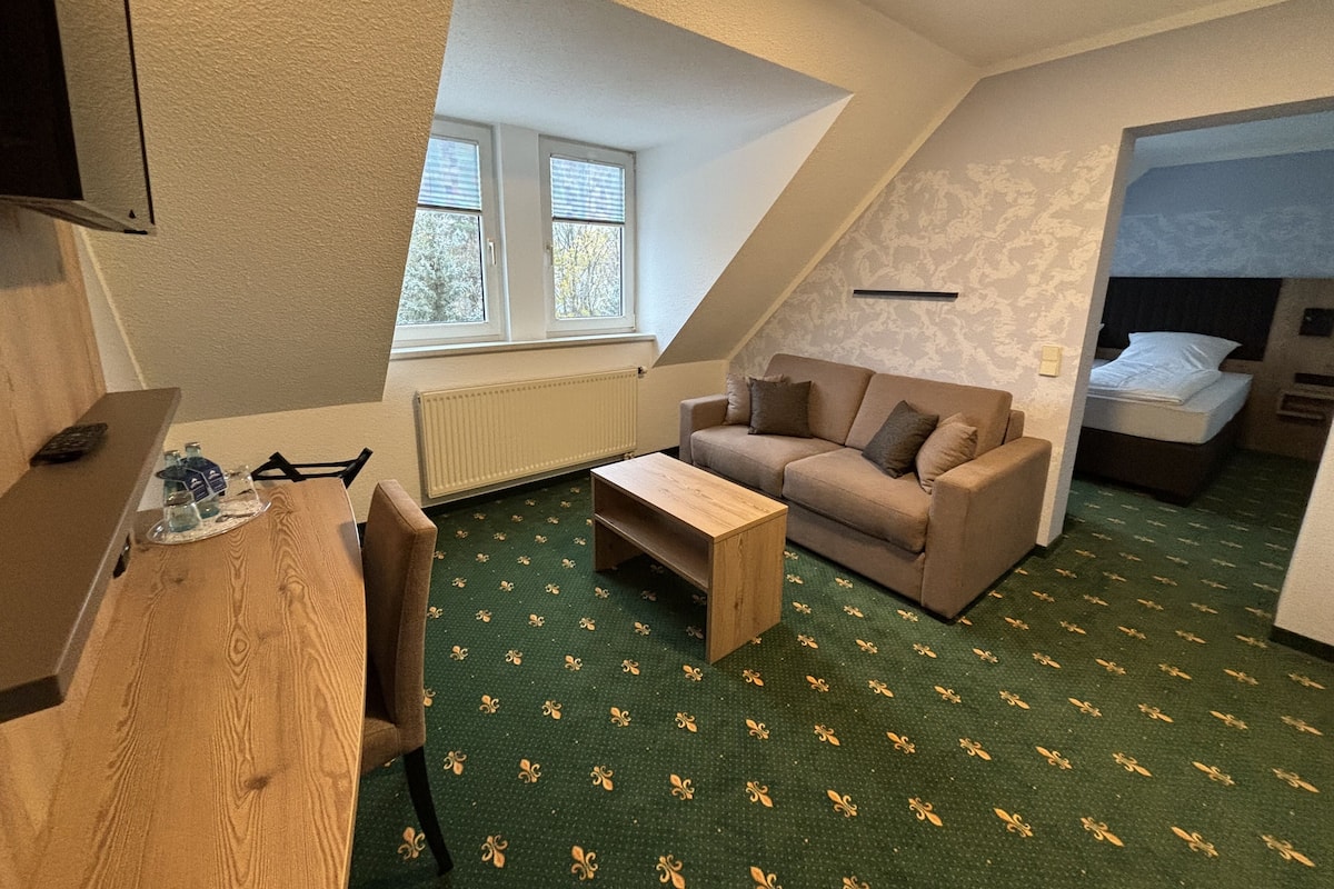 A room with a wooden desk, a sofa, a radiator, and a window.