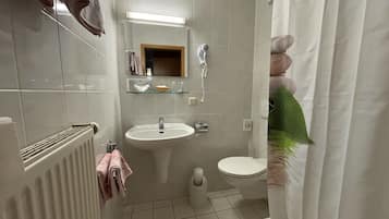 A bathroom with a white sink, toilet, and shower. There is a towel rack with towels, a mirror, and a shelf with toiletries.