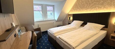 A hotel room with two beds, a desk, a chair, a window with blinds, and a radiator.