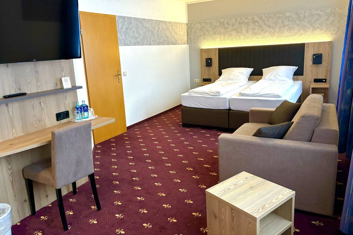 A hotel room with a TV, a desk, a bed, and a sofa.