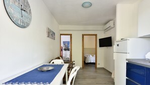 A modern kitchen with a dining area, white cabinets, a blue countertop, and a wall clock. - Casa Cala Sisine (Baunei)