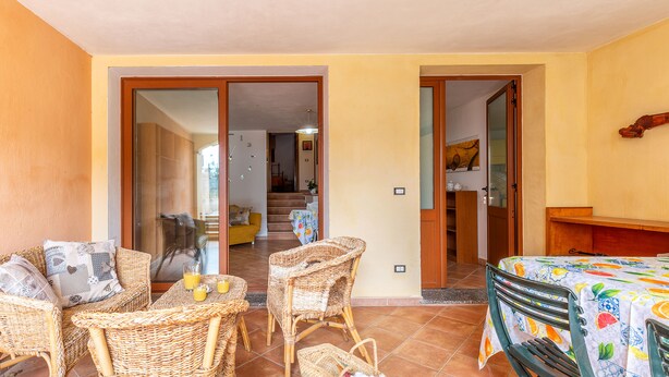 Un patio con mobiliario de mimbre, una mesa con mantel estampado de frutas y vista hacia el interior de la casa.