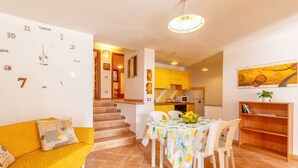 Un comedor con una mesa preparada para cuatro personas, un sofá amarillo y un reloj de pared.
