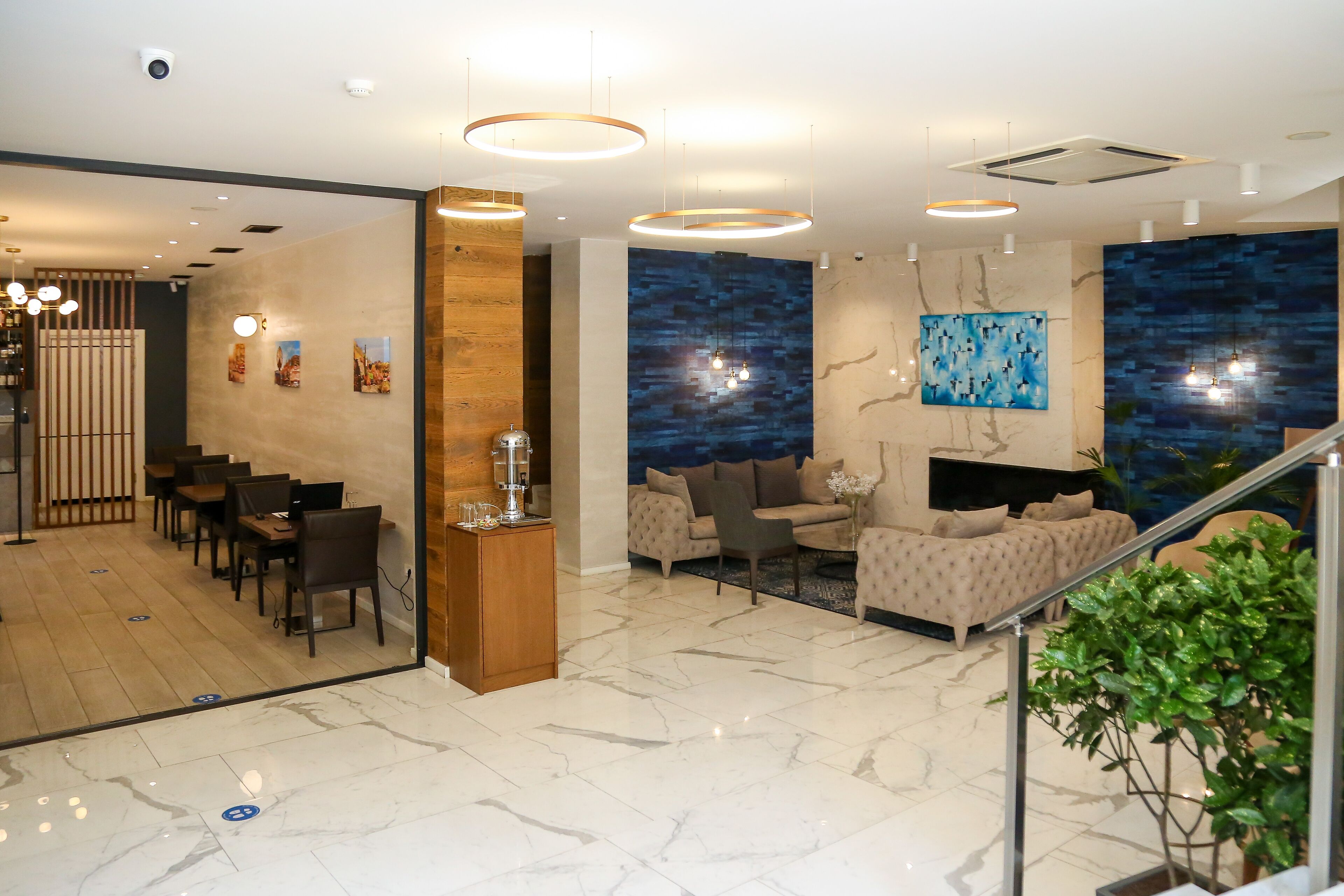 Un hall d’hôtel moderne comprenant un espace repas, des sièges disposés autour d’une cheminée et un escalier.