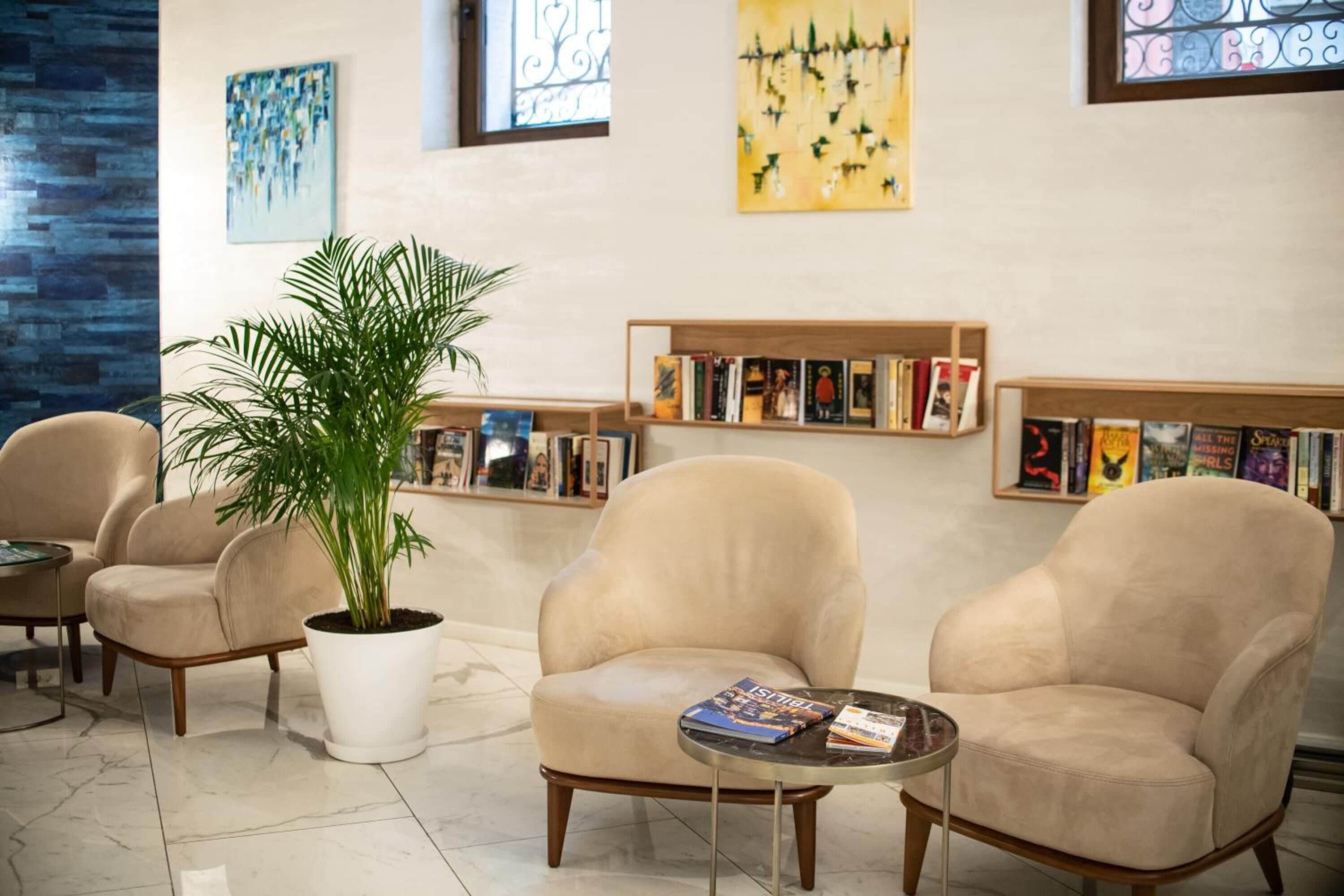 Un área de descanso moderna con sillones color beige, una planta en maceta y estanterías llenas de libros.