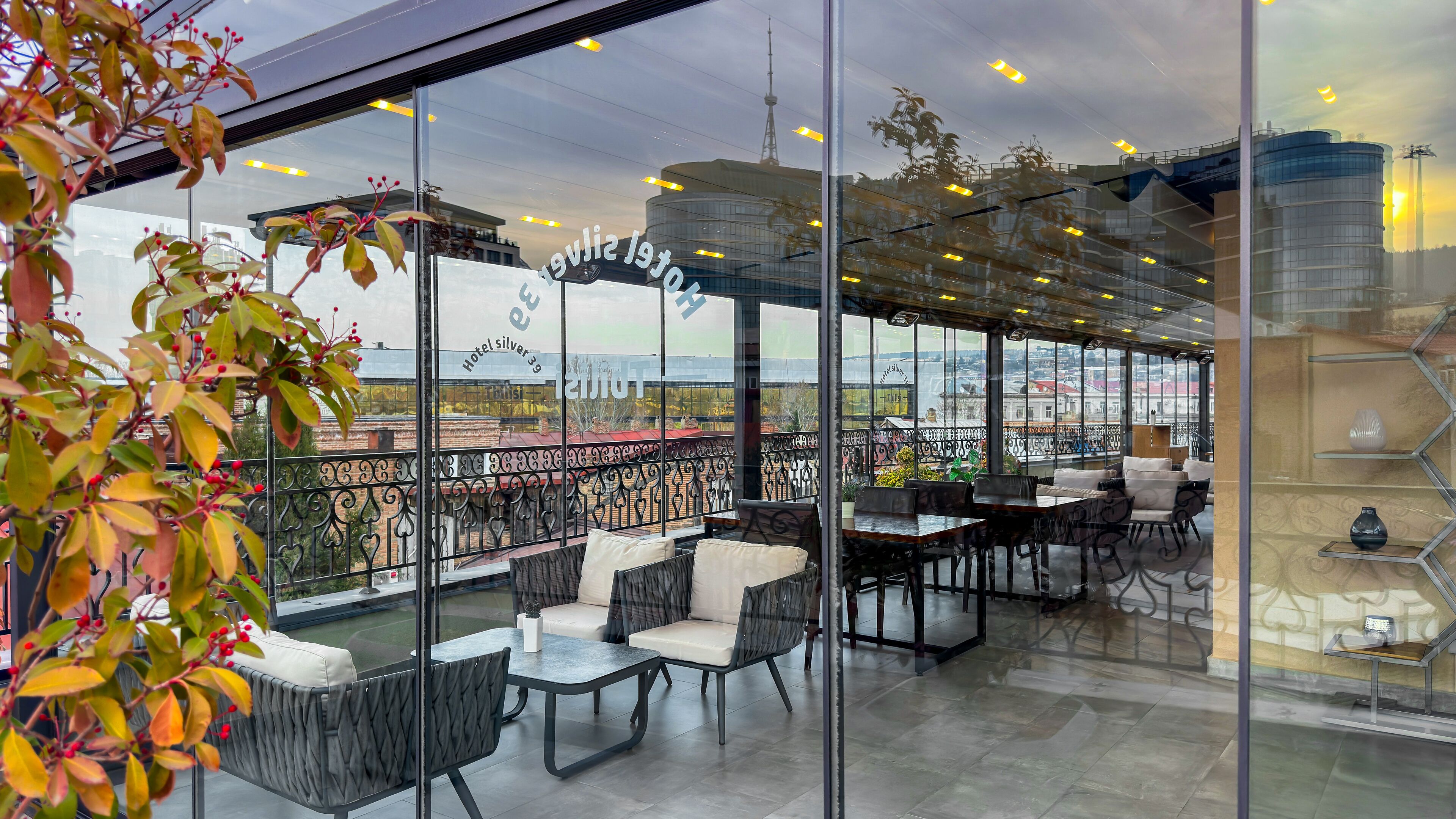 A modern outdoor seating area with glass walls, wicker furniture, and a view of the cityscape.