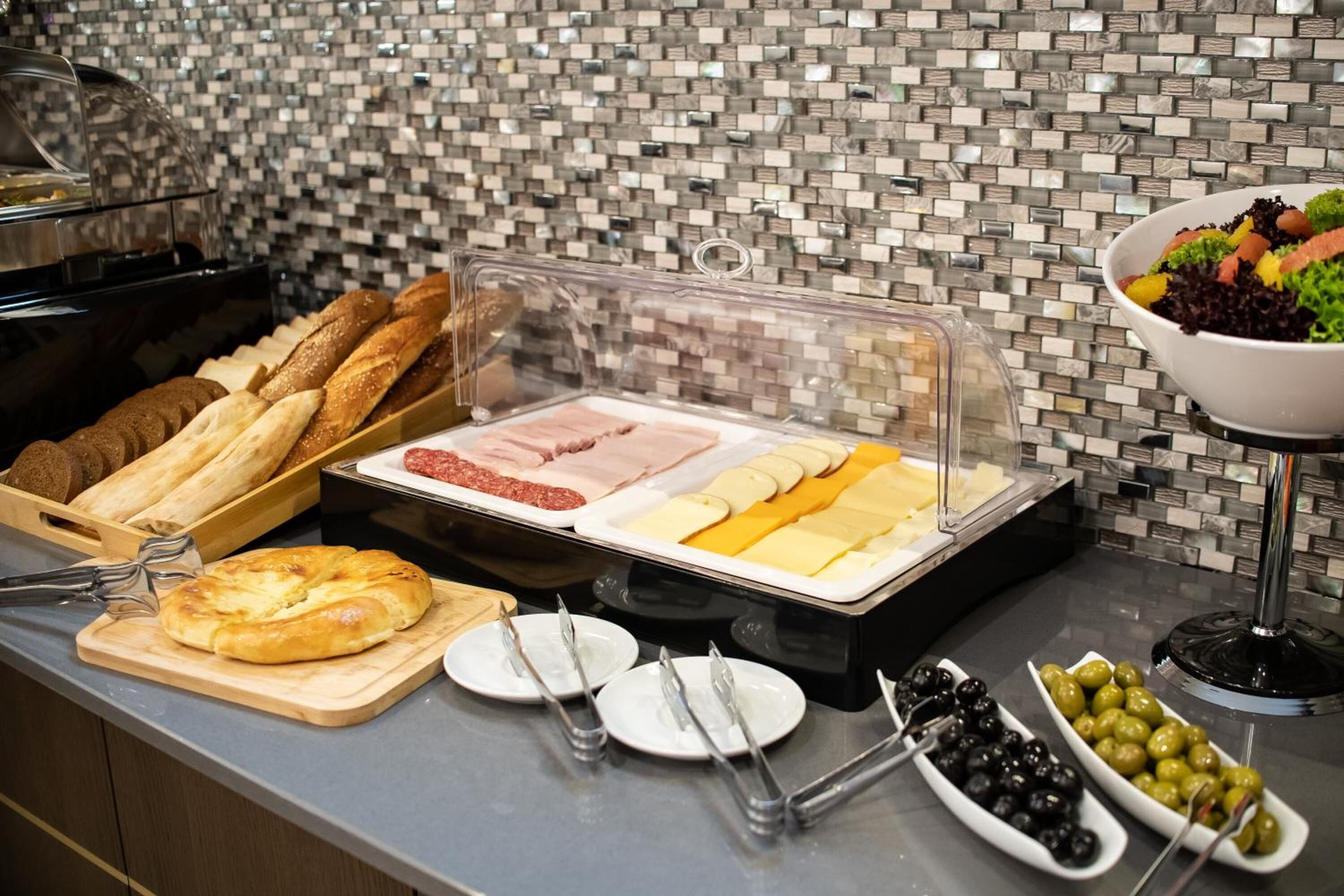 A buffet with various food items including bread, meats, cheeses, and olives.