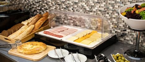 A buffet with various food items including bread, meats, cheeses, and olives.