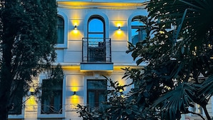 Een meerlaags gebouw met balkons, verlicht met warme verlichting, omgeven door groen.