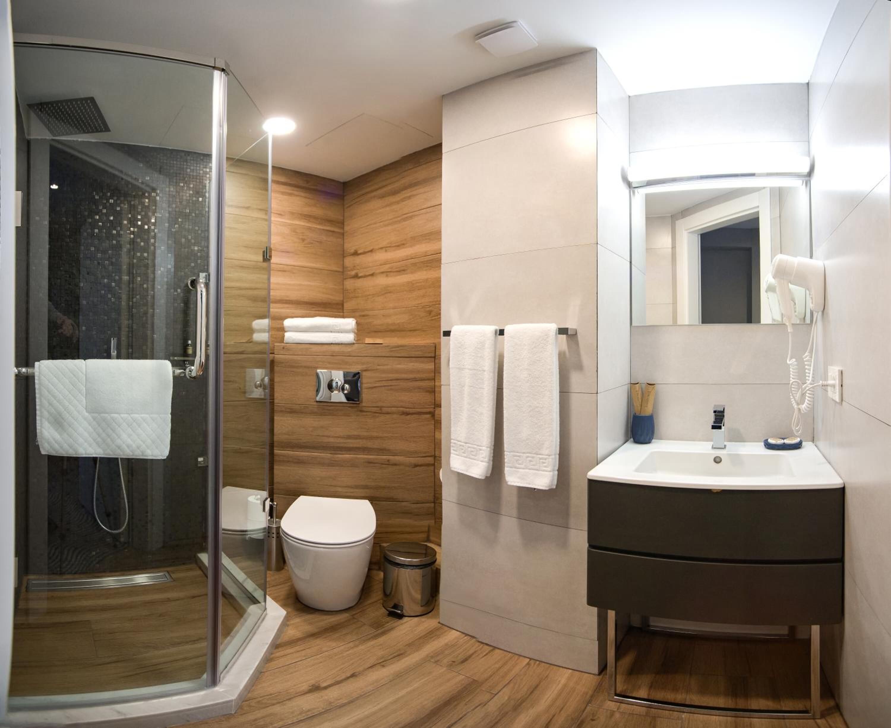 A modern bathroom with a glass shower enclosure, a toilet, a sink with a mirror, and wooden wall panels.