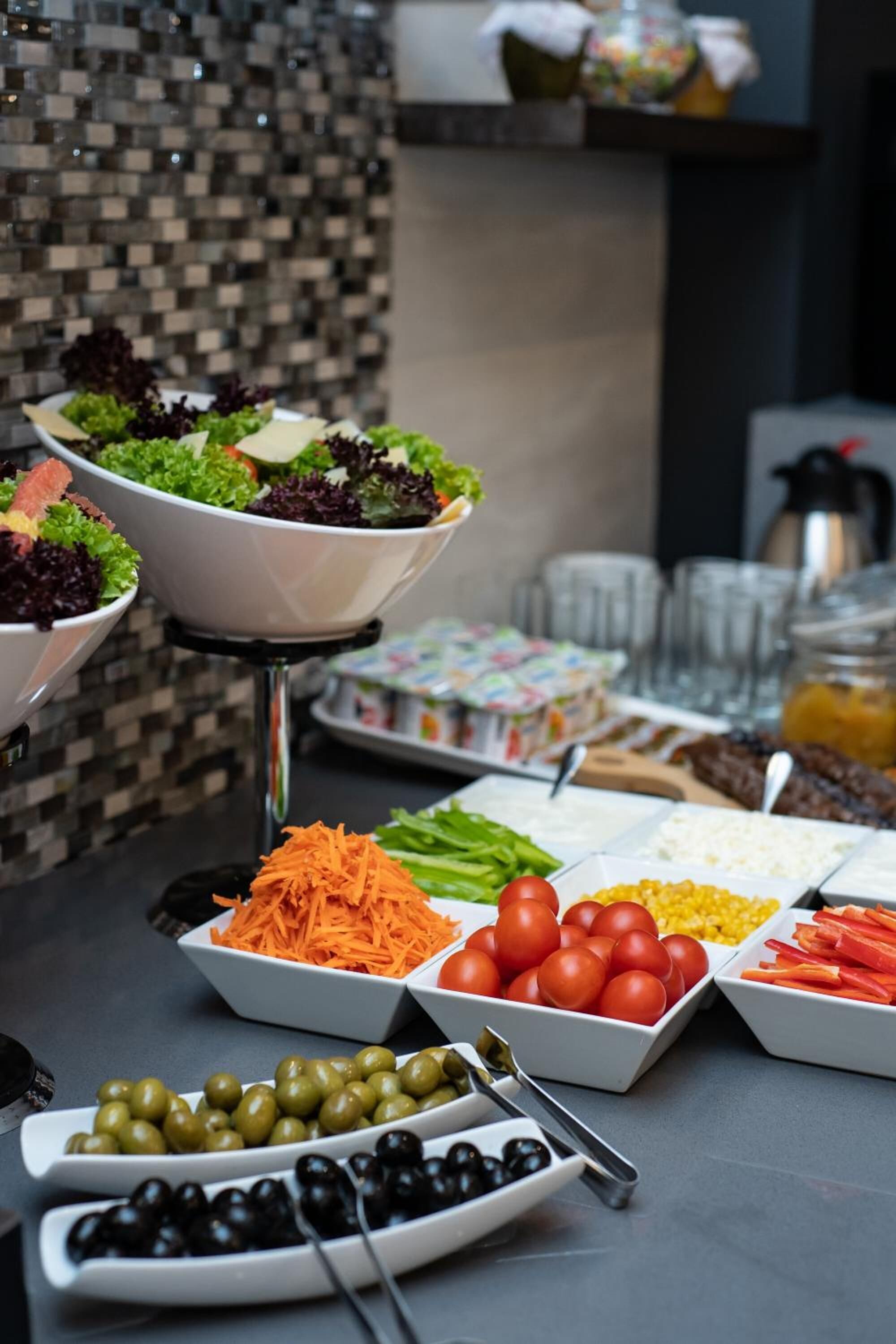 A buffet table with various food items including salads, vegetables, and olives.