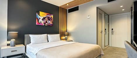 A modern hotel room with a large bed, two bedside tables with lamps, a colorful abstract painting on the wall, a wooden panel design, and a door with a lock.