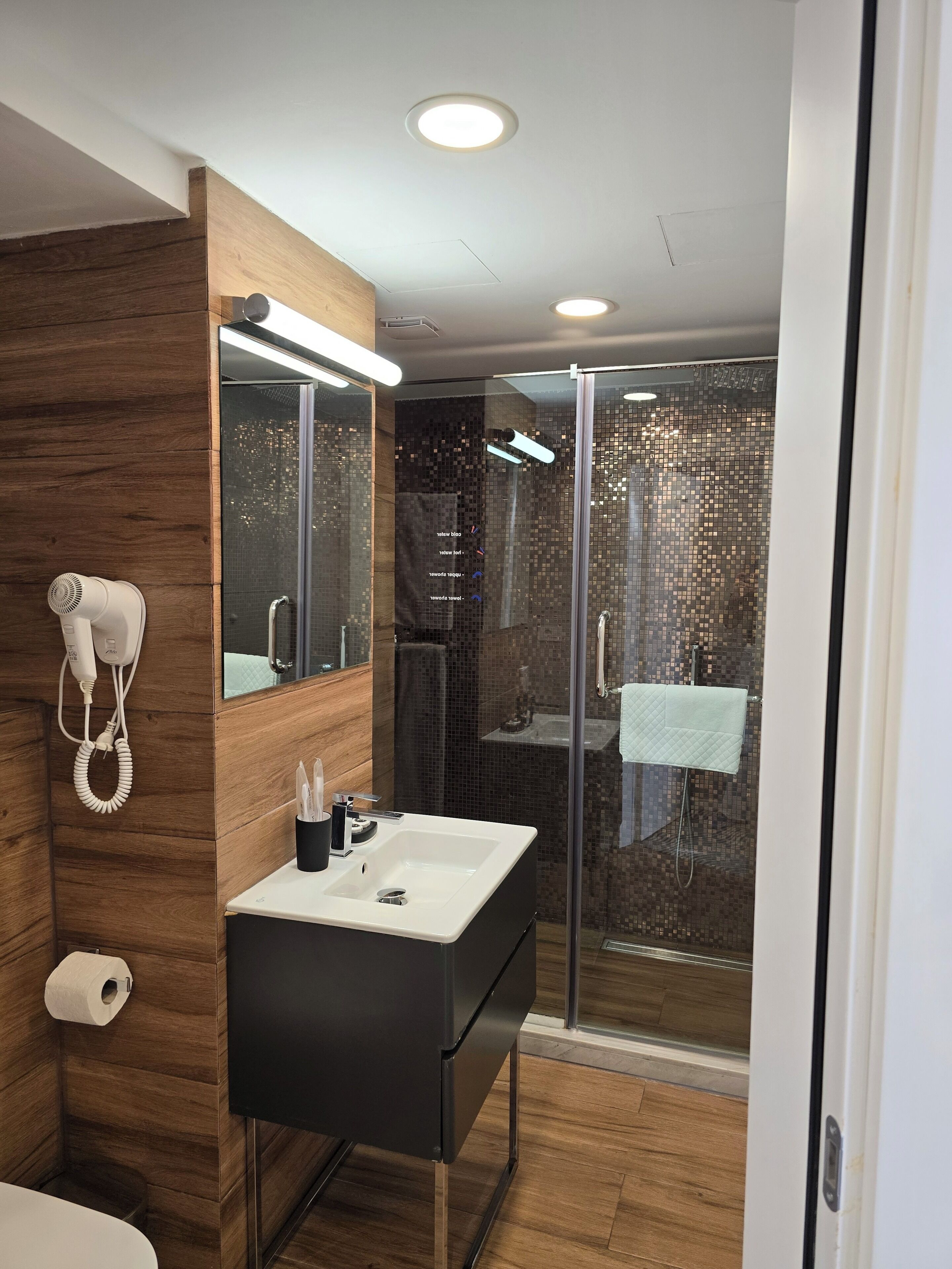 A modern bathroom with a wooden vanity, a glass shower enclosure, and a hairdryer mounted on the wall.