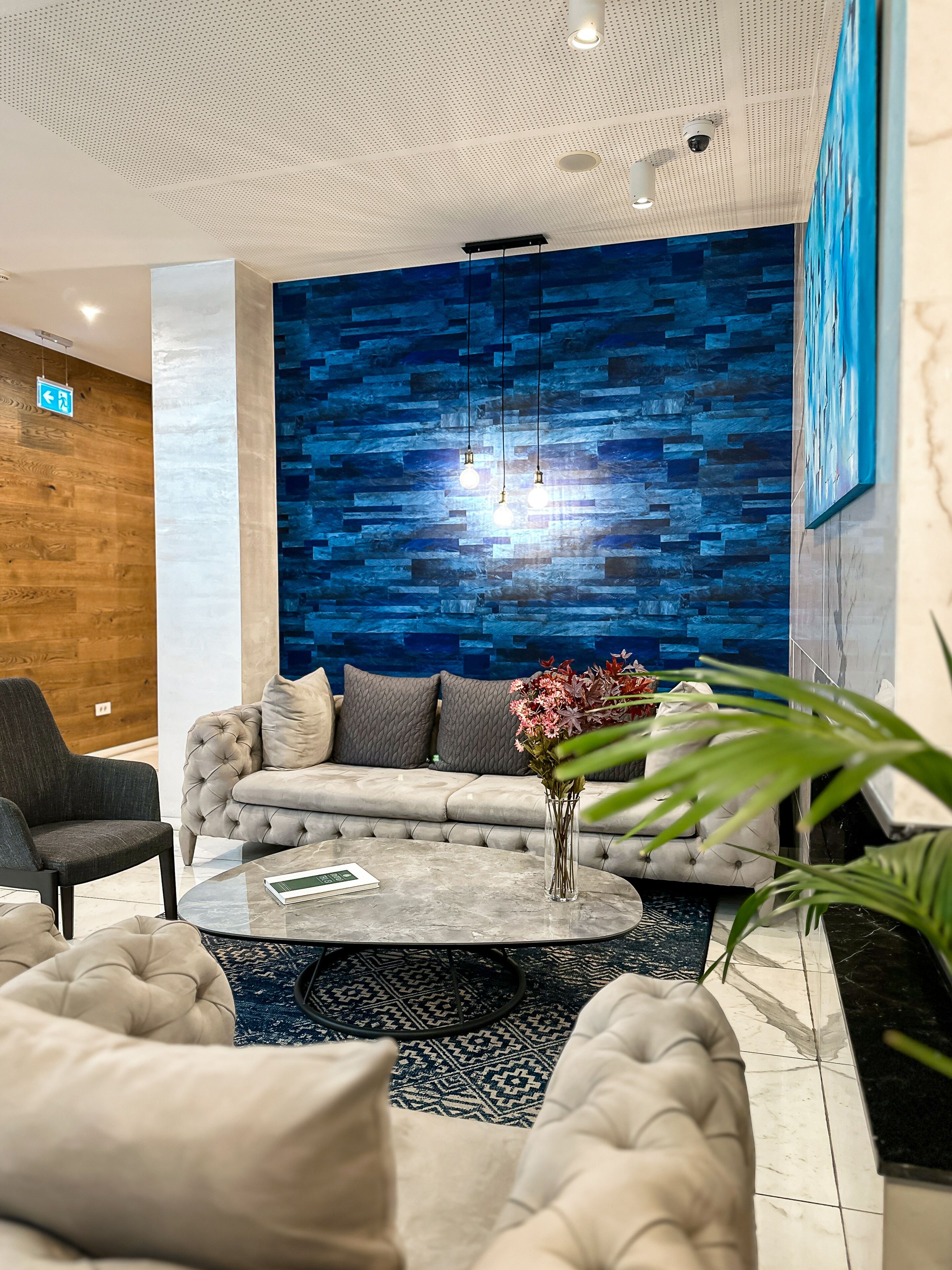 A modern lounge area with a tufted sofa, a round coffee table, and a blue patterned wall.
