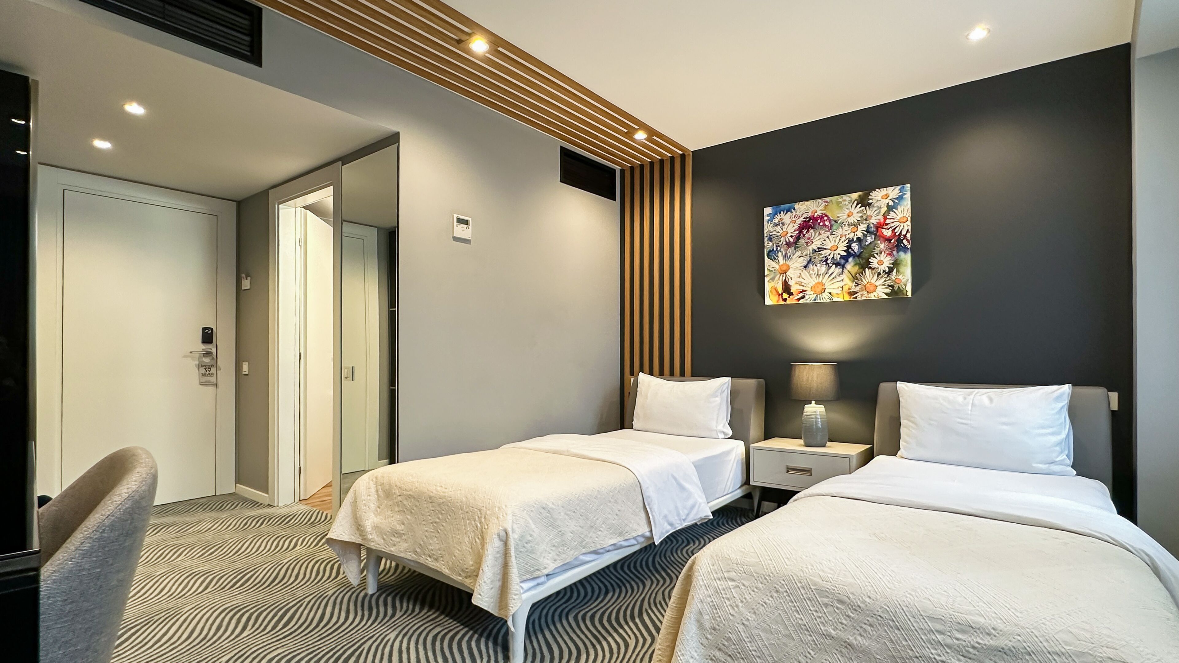 A modern hotel room with two beds, a desk, and a large window.