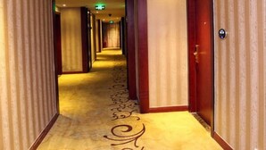 En hotellkorridor med ett mönstrat golv, trädörrar och en övervakningskamera i taket.