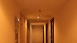En lång, smal hotellkorridor med dörrar på båda sidor och ett kaklat golv.