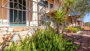 Edifici de dues plantes amb façana de pedra, escala metàl·lica i un balcó amb plantes en testos.