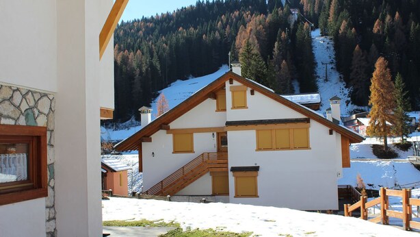 A chalet-style building with a wooden staircase leading to a balcony, surrounded by snow-covered ground and forested mountains in the background. - Casa Mazzoni (Val di Zoldo)