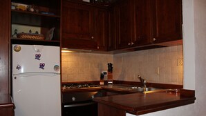 A kitchen with wooden cabinets, a white refrigerator, a stove, and a sink. - Casa Mazzoni (Val di Zoldo)