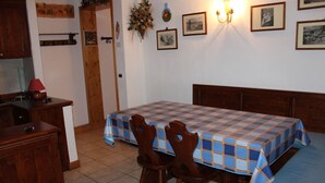 A room with a bed, a table with chairs, a wooden cabinet, and a wall with framed pictures and a wall sconce. - Casa Mazzoni (Val di Zoldo)