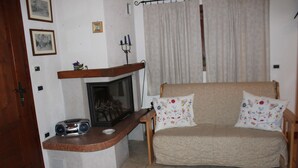 A cozy living room with a fireplace, a sofa with floral cushions, and a radio on a wooden console. - Casa Mazzoni (Val di Zoldo)