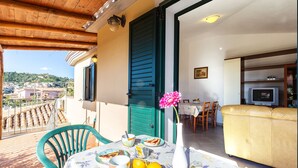 A balcony with a table set for breakfast, a sofa, and a TV in the background. - Residence Verde Navarrese B (Baunei)