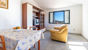 A dining area with a table set for two, a sofa, a TV, and a bookshelf. - Residence Verde Navarrese B (Baunei)