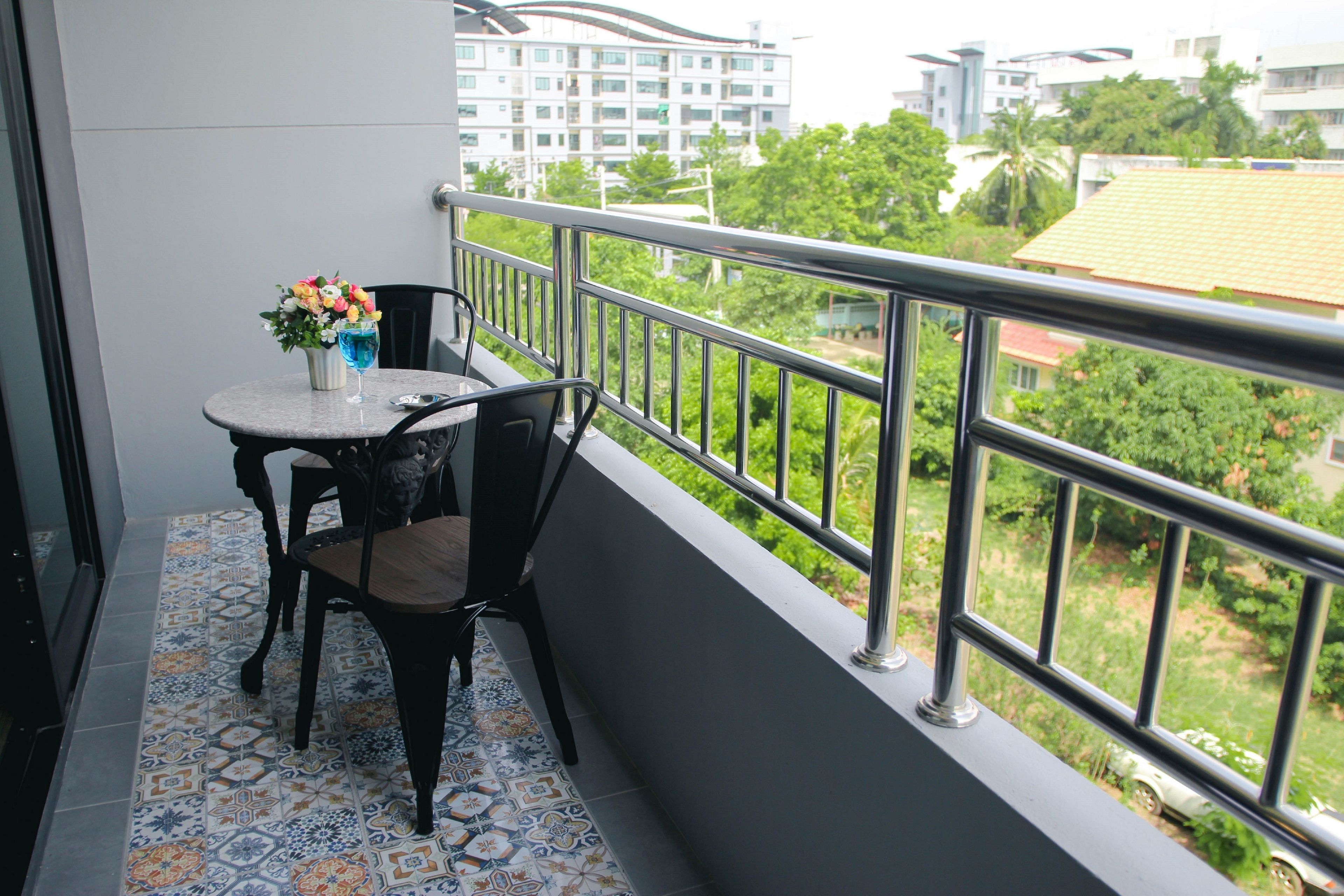 A balcony with a table and chairs, a vase of flowers, and a view of buildings and greenery.