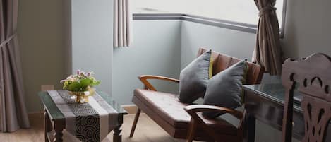Une pièce d’angle avec un banc en bois, une petite table recouverte d’une nappe à motifs et une fenêtre avec des rideaux.