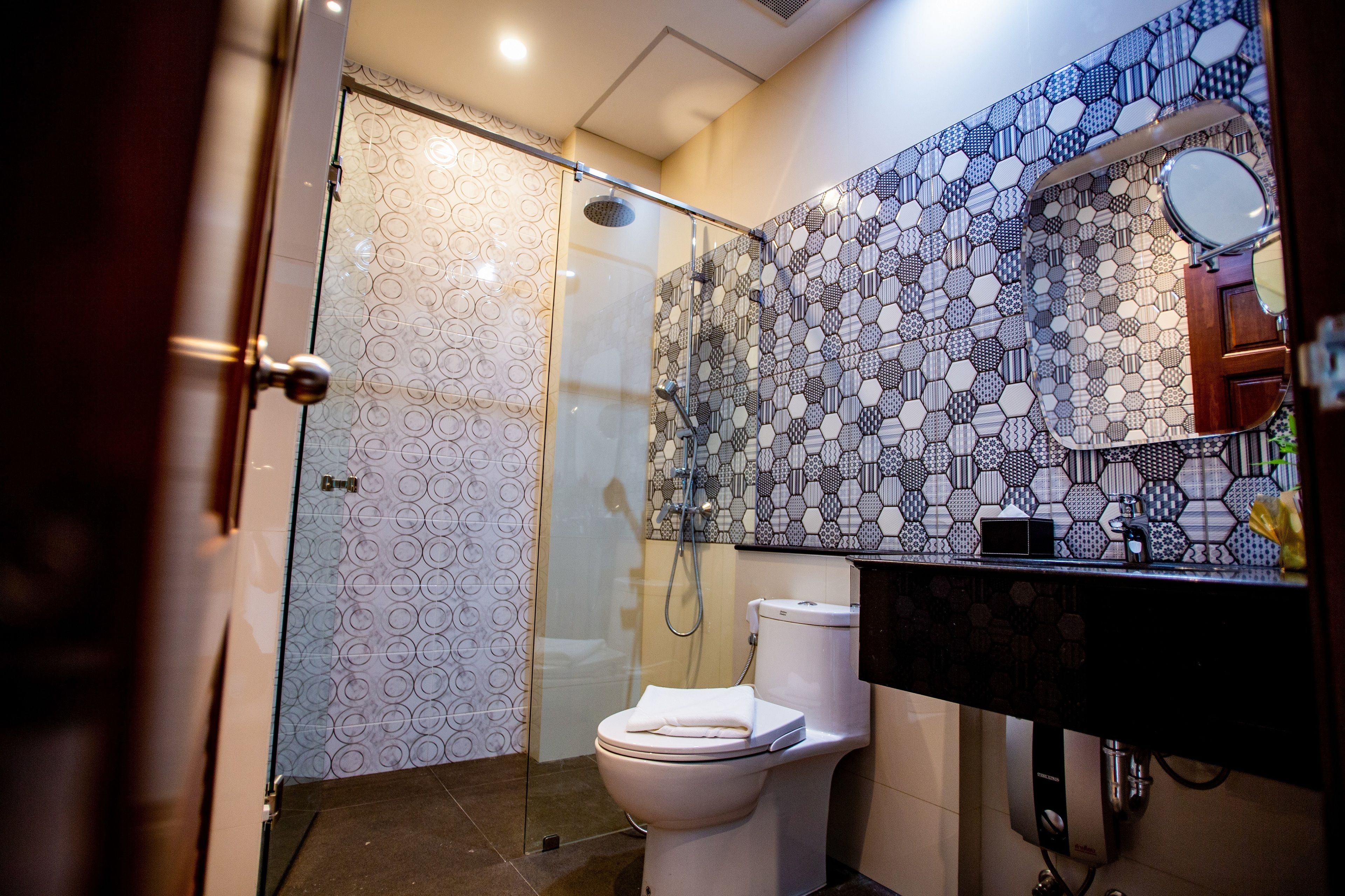Een moderne badkamer met een douchecabine van glas, een wit toilet en een zwarte wastafel met een spiegel erboven.