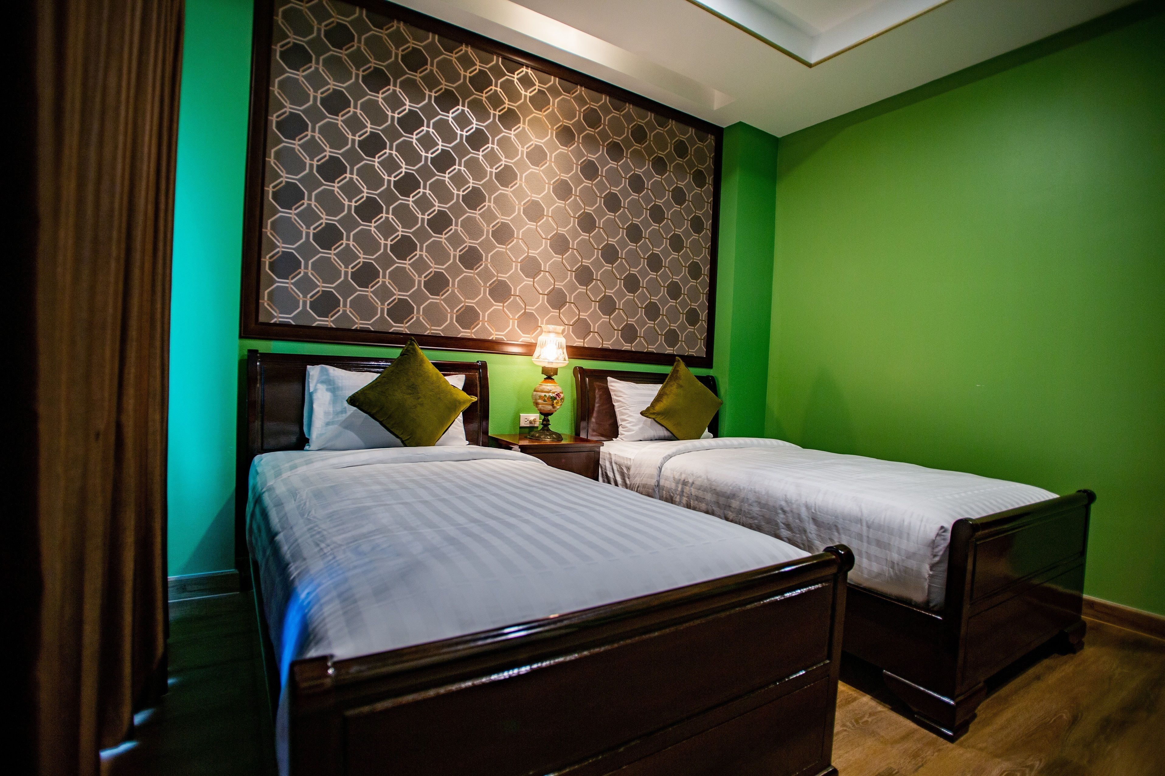 A room with two beds, a patterned headboard, and a green wall.
