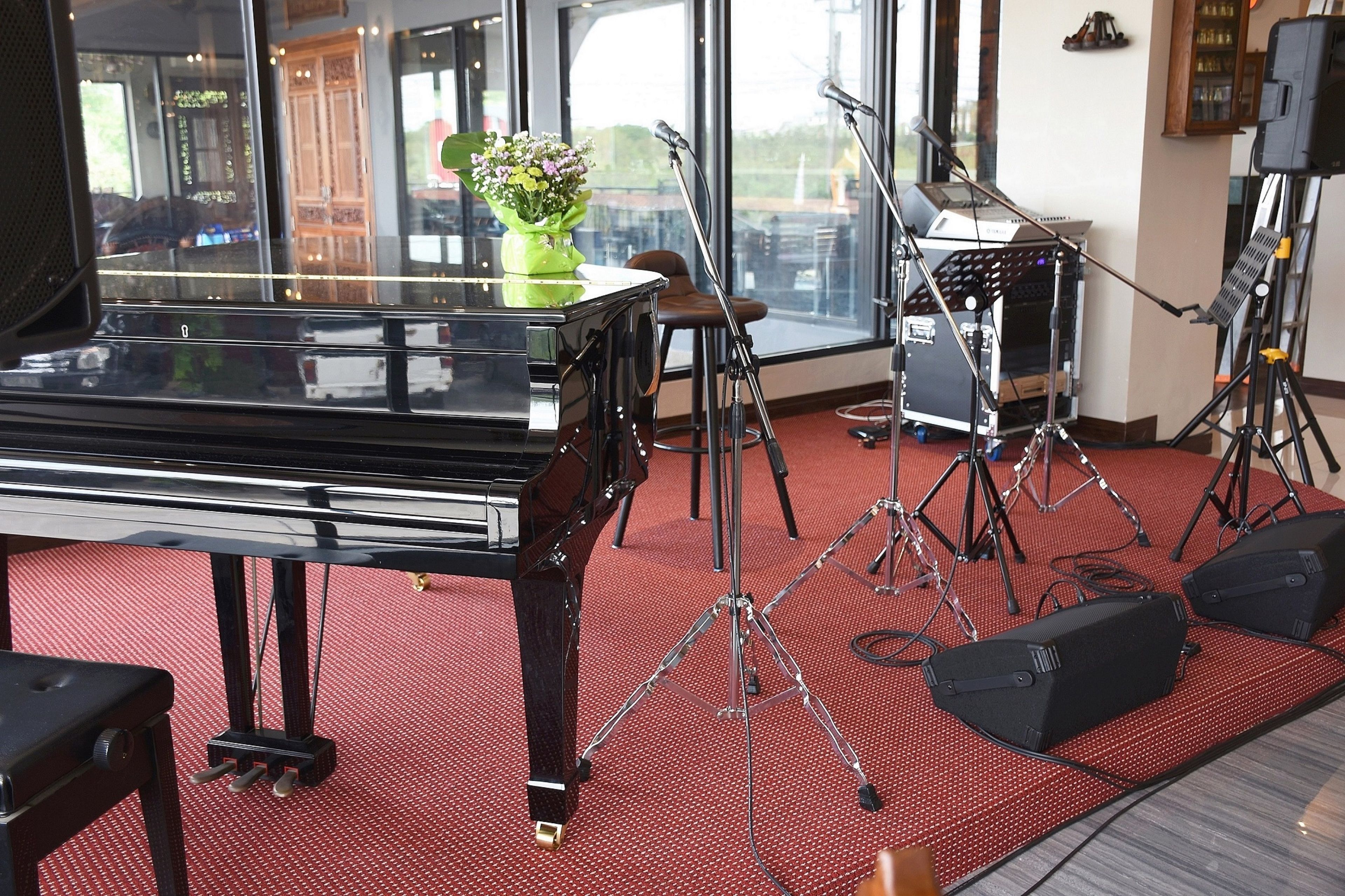 A piano, microphones, and speakers in a room with a red carpet and large windows.