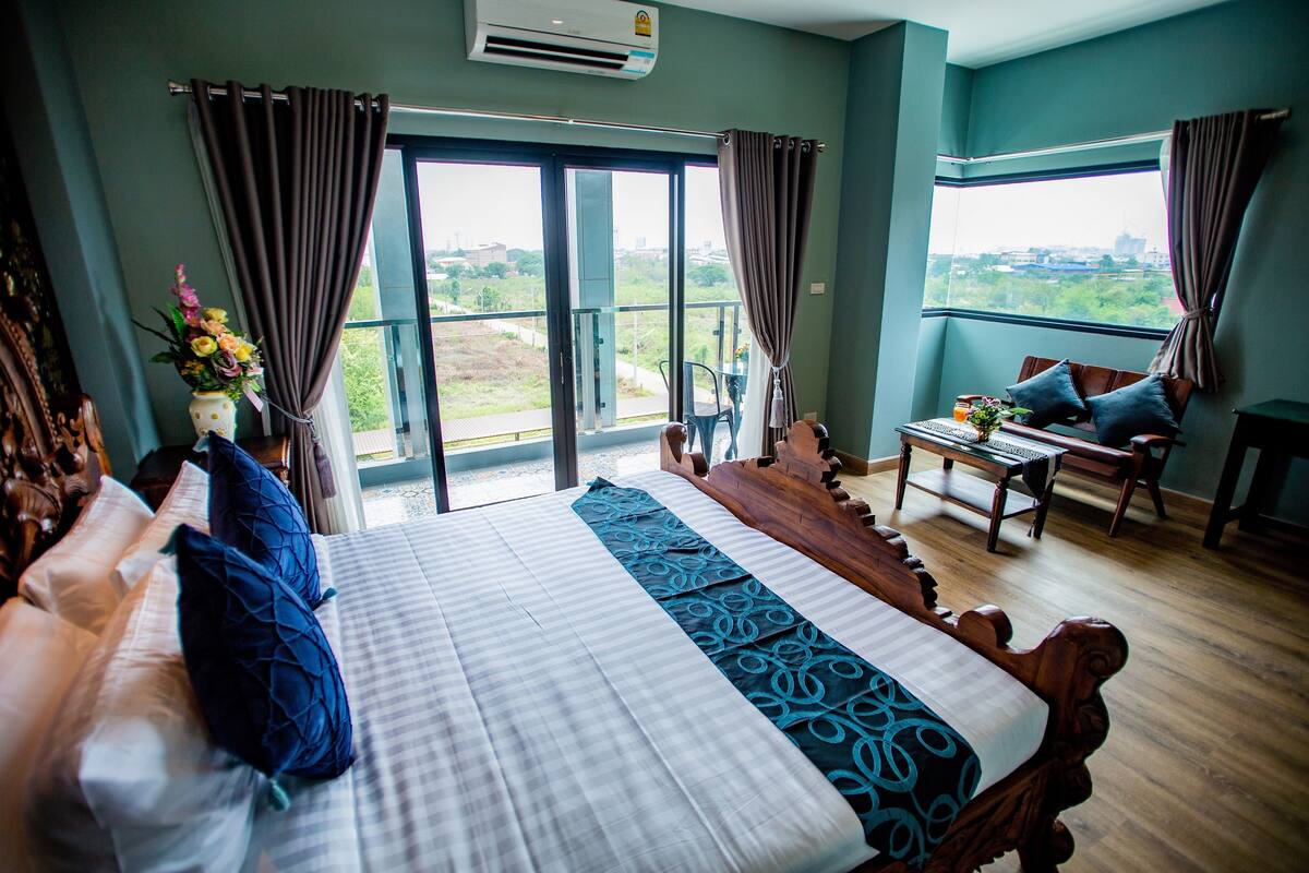A hotel room with a large bed, a small table with a chair, and a balcony with a view.