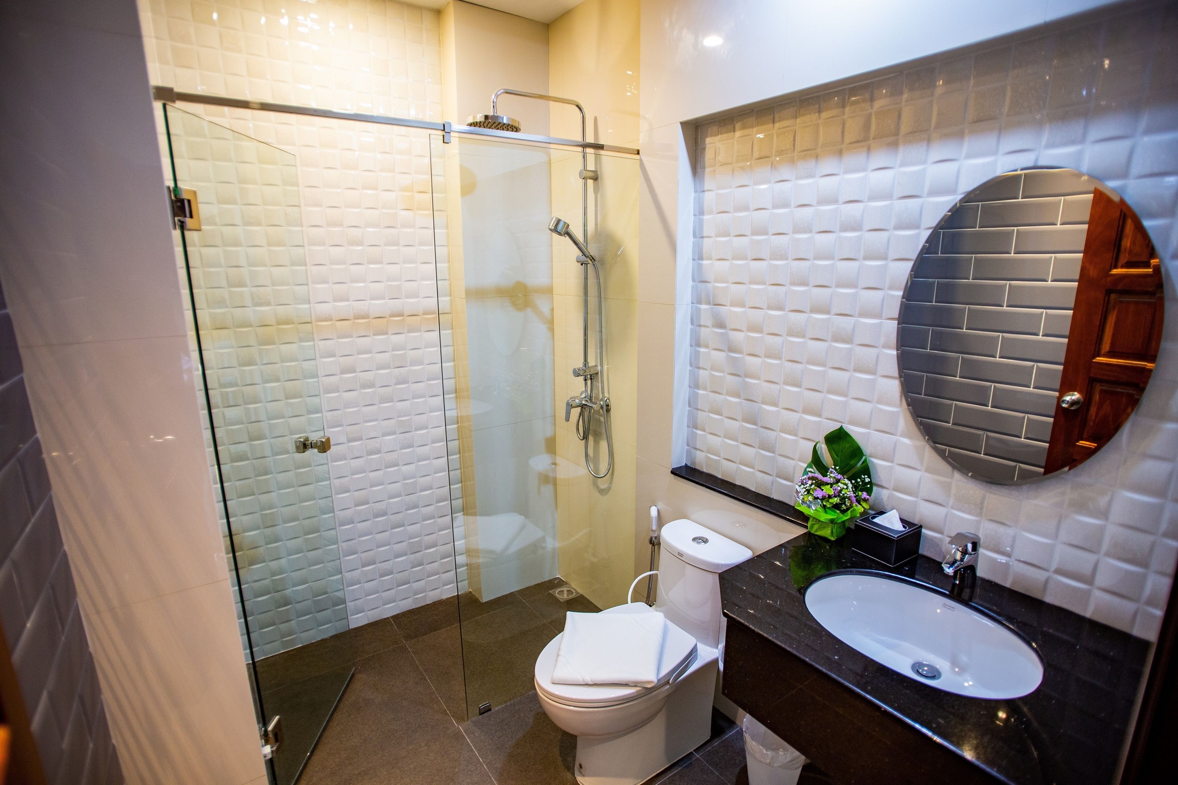 A modern bathroom with a glass shower enclosure, a white toilet, and a black sink with a mirror above it.