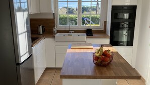 Una cocina moderna con armarios blancos, encimera de madera, horno Bosch y ventana con vista a zonas verdes.